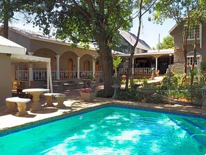A pool area with a clear blue pool, stone seating, and a covered patio with arches. - Hobbit Boutique Hotel (Bloemfontein)