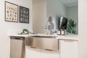 Eine moderne Küche mit einem Edelstahl-Geschirrspüler, einem Waschbecken mit Armatur und zwei gerahmten Pflanzenbildern an der Wand.