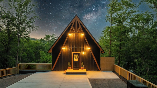A wooden cabin with a triangular roof, a porch, and a starry night sky. - Luxury A-Frame w/ Hot Tub (Sevierville)