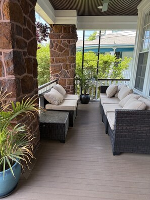 A covered porch with wicker furniture, stone pillars, and potted plants.