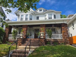 A two-story house with a stone facade, a front porch with steps, and a bay window.
