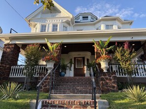 A two-story house with a front porch, stone pillars, and a staircase leading to the entrance. - Elegant Apartment in Asbury Park Mansion - Central Location near Stone Pony (Asbury Park)