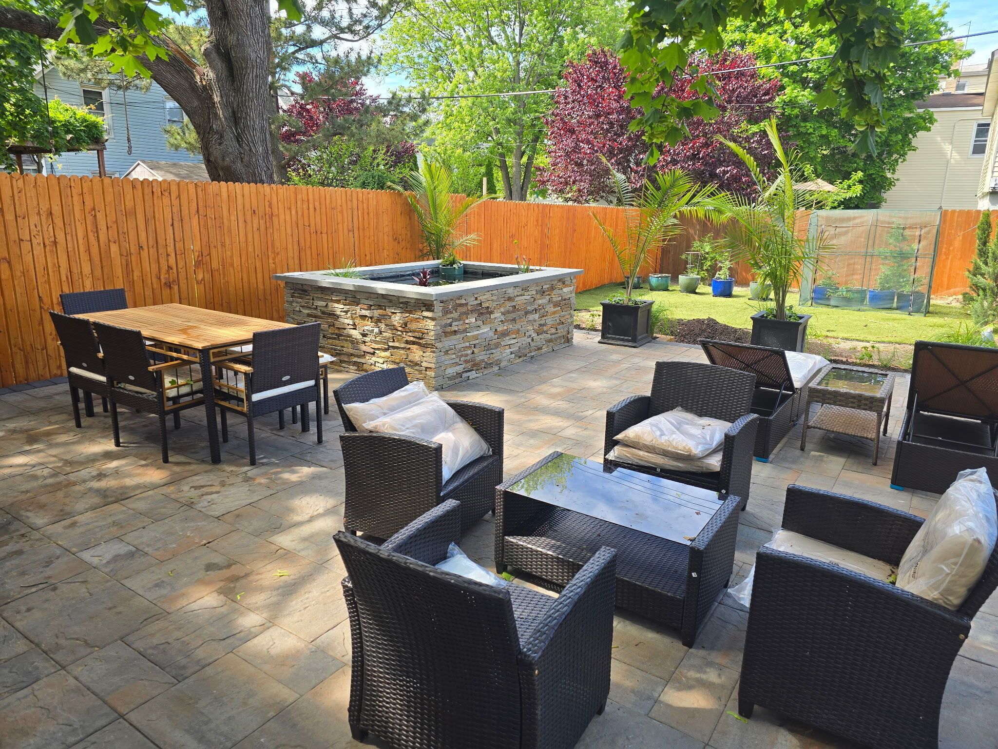 Une terrasse extérieure avec un foyer en pierre, des meubles en osier et une clôture en bois.