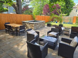 An outdoor patio with a stone fire pit, wicker furniture, and a wooden fence. - Elegant Apartment in Asbury Park Mansion - Central Location near Stone Pony (Asbury Park)