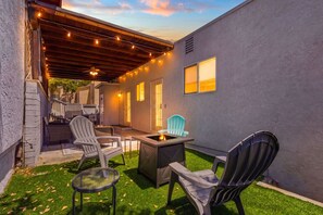 Eine Terrasse mit Gartenmöbeln, einem Feuerkorb und Lichterketten.
