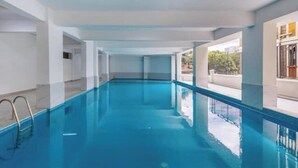 Una amplia piscina interior con agua cristalina y paredes y columnas blancas.