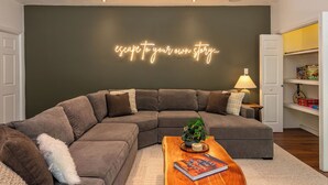 Ein modernes Wohnzimmer mit einem Ecksofa, einem Couchtisch mit einem Buch und einer Neonleuchtreklame an der Wand.