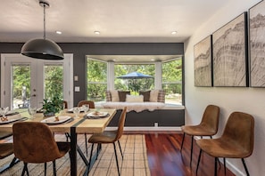 A dining area with a bay window, wooden table, chairs, and a hanging light fixture. - The Fable House | Sequoia Riverfront Modern Design (Three Rivers)