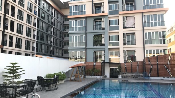 A modern building with multiple balconies, a swimming pool, and outdoor seating. - Central Mansion (Bangkok)