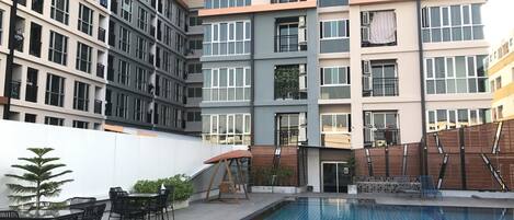 A modern building with multiple balconies, a swimming pool, and outdoor seating.