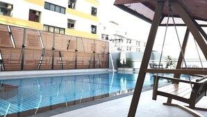 A swimming pool with a wooden deck and a view of a multi-story building with balconies. - Central Mansion (Bangkok)