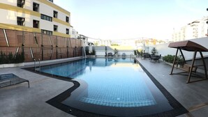 An indoor swimming pool with a tiled edge, lounge chairs, and a wooden swing. - Central Mansion (Bangkok)