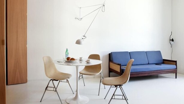 A modern room with a round table, two chairs, a blue sofa, and a hanging light fixture. - Concoct Apartment Milano (Milan)