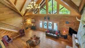 Eine Holzhütte mit Innenraumgestaltung aus Holz, einer Kandelaberleuchte, einem Kamin, einer Couch, einem Sessel und einer Treppe.