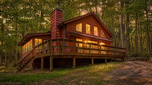 Eine Holzhütte mit einer Terrasse, einem Schornstein und einem Wald im Hintergrund.