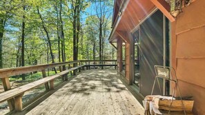 Eine Holzterrasse mit Geländer, umgeben von Bäumen, die zu einem Gebäude mit großen Fenstern führt.