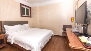 Ein Hotelzimmer mit einem Bett, einem Schreibtisch mit Wasserkocher, einem Sessel und einem Fernseher.