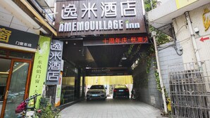 Ein Hotel Eingang mit einem Schild für AMEMOVILLAGE Inn, einem überdachten Gang und zwei parkenden Autos.