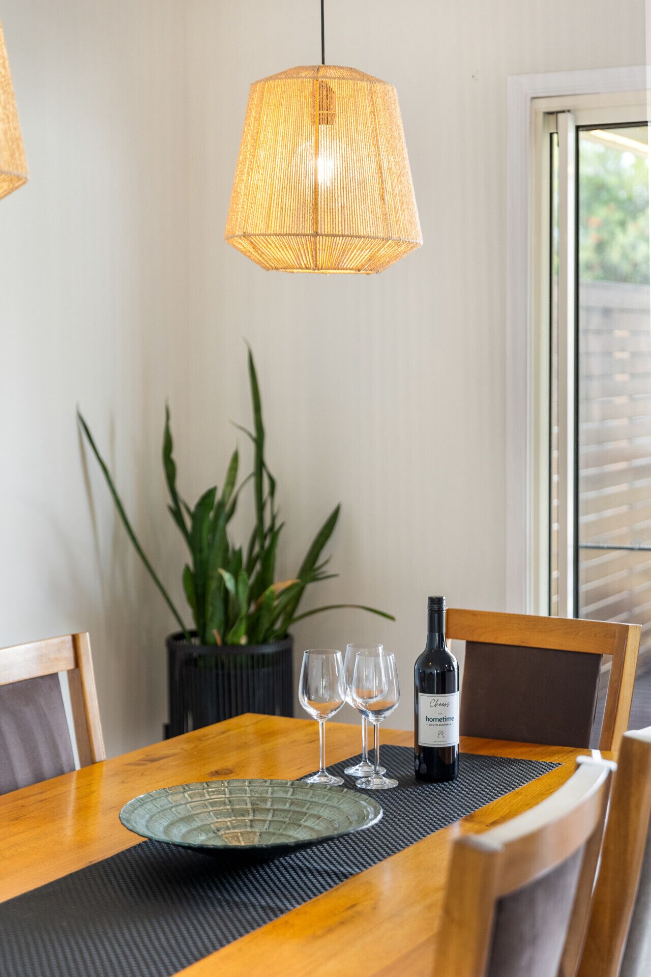 A dining table with a bottle of wine, two glasses, and a placemat.