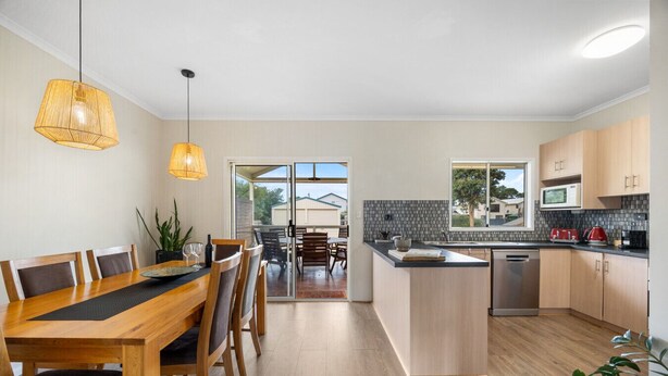 A modern kitchen with a dining area, wooden furniture, and a view through the glass door. - Salt & Stay - Laid-Back Comfort by the Beach (Encounter Bay)