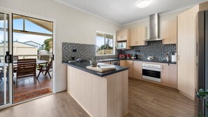 A modern kitchen with a central island, wooden cabinets, a microwave, and an oven. - Salt & Stay - Laid-Back Comfort by the Beach (Encounter Bay)