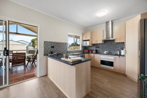 A modern kitchen with a central island, wooden cabinets, a microwave, and an oven. - Salt & Stay - Laid-Back Comfort by the Beach (Encounter Bay)