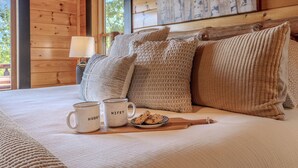 Ein Schlafzimmer in einer Holzhütte mit einem Bett, Kissen, einer Tasse und Keksen.
