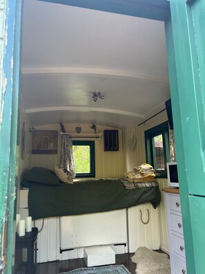 Una habitación pequeña y acogedora con una cama individual, una ventana con cortinas, una mesita con velas y un aparador.