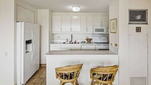 A kitchen with white cabinets, a white refrigerator, a microwave, a sink, and two wicker chairs. - 28th Floor Ala Moana Suite | City + Mountain Views (Honolulu)