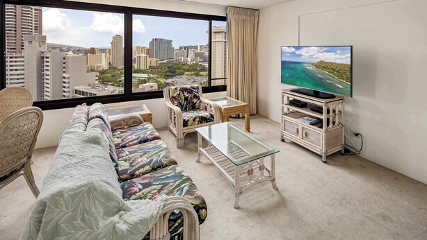 A hotel room with a large window, a sofa, a glass coffee table, a television, and a small table with a TV stand. - 28th Floor Ala Moana Suite | City + Mountain Views (Honolulu)
