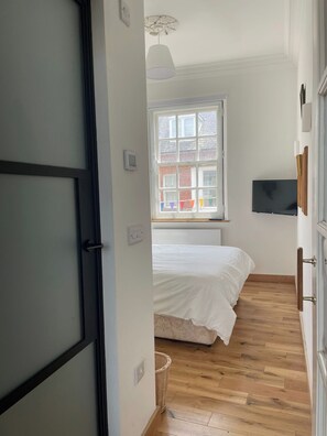 A bedroom with a bed, a window, a TV, and a door.