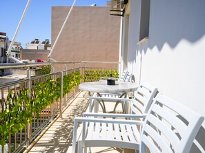 Terraza en la azotea con una mesa redonda y sillas blancas, rodeada por una barandilla de metal y plantas verdes.