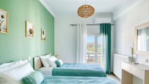 Ein Schlafzimmer mit zwei Betten, einem Fenster mit Vorhängen, einem Heizkörper und einer Pendelleuchte.