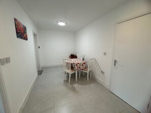 A small, clean room with a tiled floor, a white door, and a table with chairs. - Apartment Sleeps 2 with Parking (Hayes)