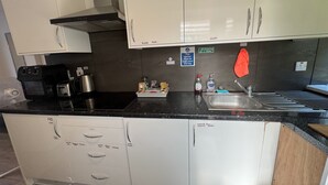 Cozinha com armários brancos, bancada preta, cafeteira, chaleira e pia.