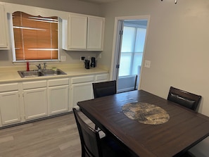 Una cocina con armarios blancos, un lavabo y una mesa de comedor con sillas.