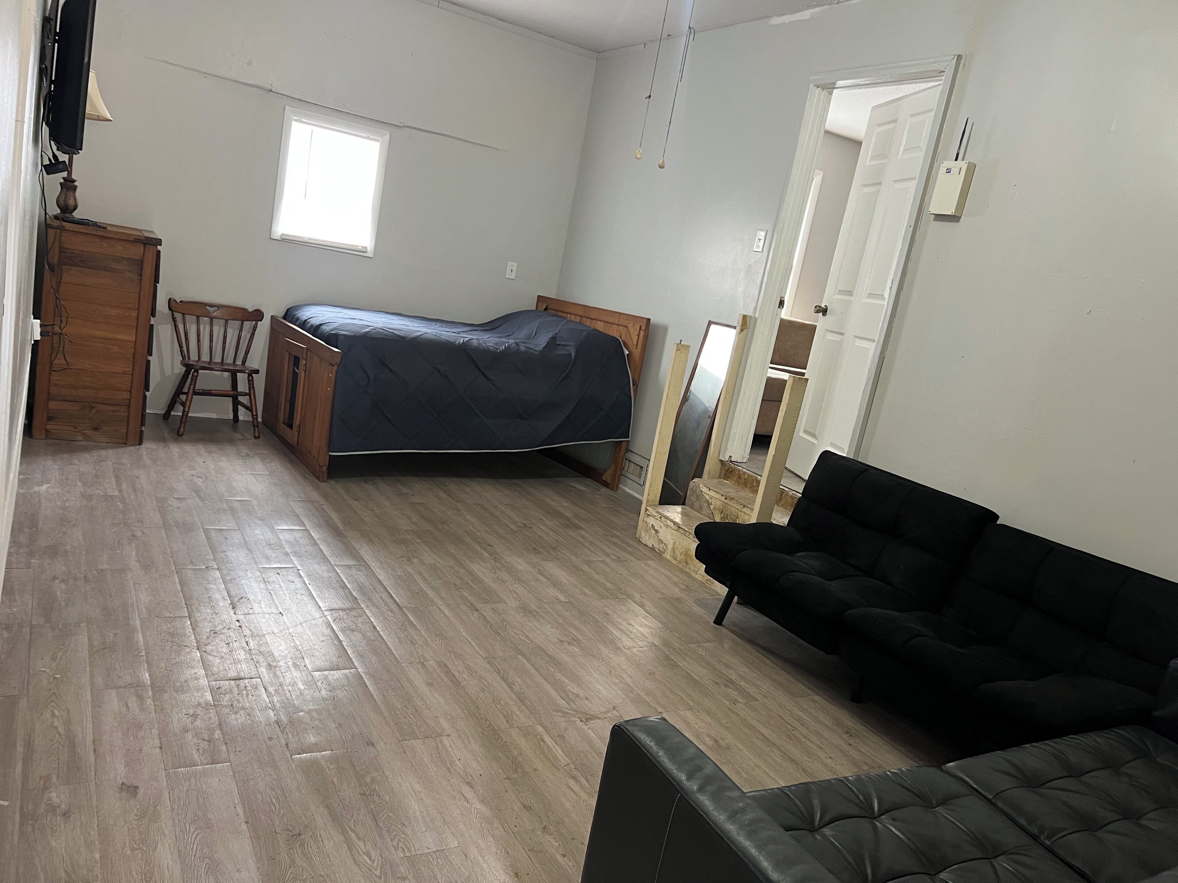 A bedroom with a bed, a wooden chair, a black sofa, and a wooden cabinet.