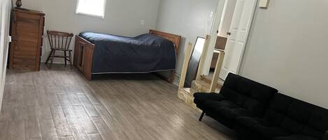 A bedroom with a bed, a wooden chair, a black sofa, and a wooden cabinet.