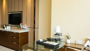 Ein Hotelzimmer mit Holzschrank, Flachbildfernseher, Glastisch und kleiner Topfpflanze.