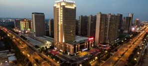Un edificio de gran altura con varios pisos, rodeado de otros edificios altos, y una calle concurrida con automóviles y letreros iluminados.