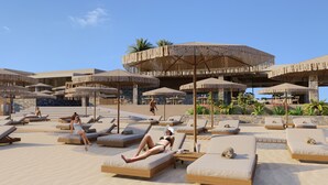 A resort with outdoor lounge areas, umbrellas, and a stone building in the background. - Unique Blue Resort (Hersonissos)