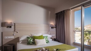 A hotel room with a bed, bedside lamps, a small table, a tray with tea and cups, and a view of the outside. - Unique Blue Resort (Hersonissos)