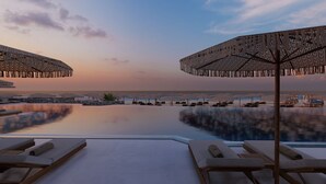 A poolside area with lounge chairs and umbrellas, overlooking a calm body of water and distant shoreline. - Unique Blue Resort (Hersonissos)