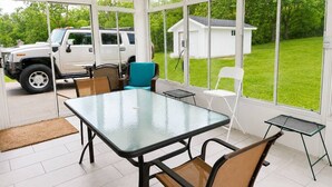 En overdækket terrasse med et glasbord, stole og en bil parkeret udenfor.
