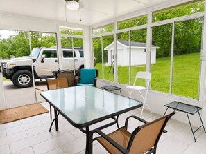 Ein überdachter Patio-Bereich mit einem Glastisch, Stühlen und einem geparkten Fahrzeug.