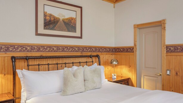 A neatly made bed with white linens and fluffy pillows, a framed picture on the wall, and a wooden door.