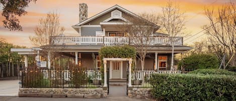 A two-story house with a porch, a stone chimney, and a gated entrance.