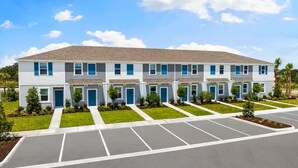 A multi-story building with a uniform facade, a parking lot in front, and small landscaped areas between the units. - Furnished Model Home – Skye Ranch (Sarasota)