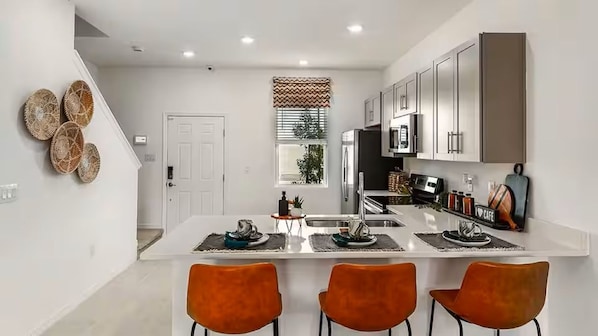 A modern kitchen with a central island, white cabinetry, and orange chairs. - Furnished Model Home – Skye Ranch (Sarasota)
