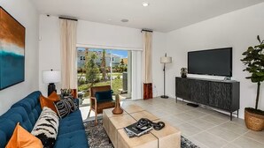 A modern living room with a sofa, coffee table, TV, and a view of the outdoors. - Furnished Model Home – Skye Ranch (Sarasota)